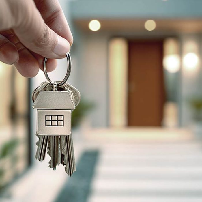 hands holding a set of house keys with a stylish home-shaped keychain in front of a newly opened home door, warm inviting lighting, modern architecture, real estate purchase concept