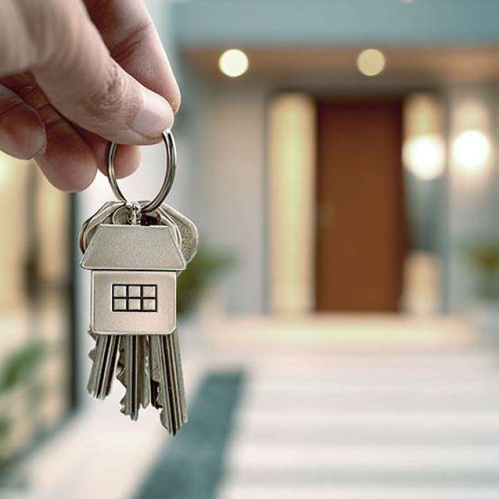 hands holding a set of house keys with a stylish home-shaped keychain in front of a newly opened home door, warm inviting lighting, modern architecture, real estate purchase concept